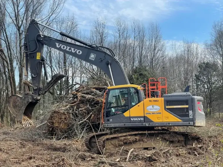 Close-up of a powerful rotary disc forestry mulcher attachment with massive sharpened steel blades for shredding vegetation, caked with wood pulp, over organic ground cover.