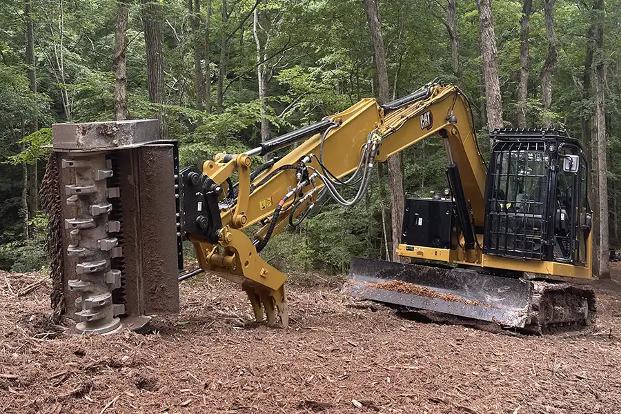 Aerial drone photograph of a large, cleared plot of ground prepared for building, surrounded by dense green forest.