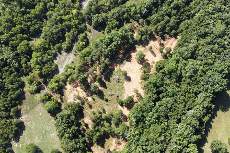 Aerial drone view of a cleared plot of dirt surrounded by dense green forest.